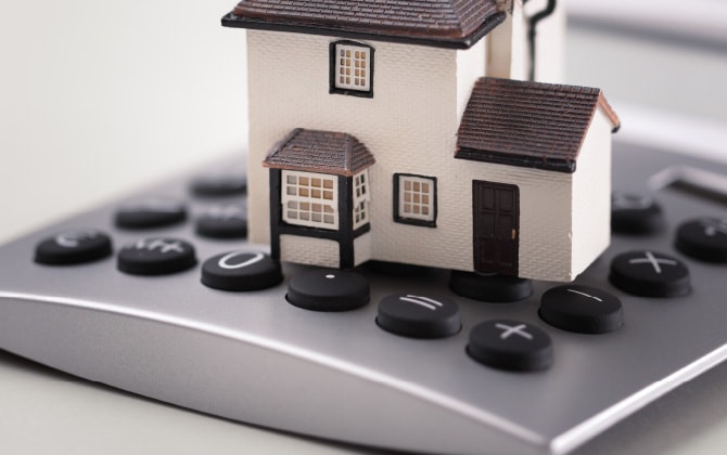 電卓の上に小さな家のオブジェが置いてある様子